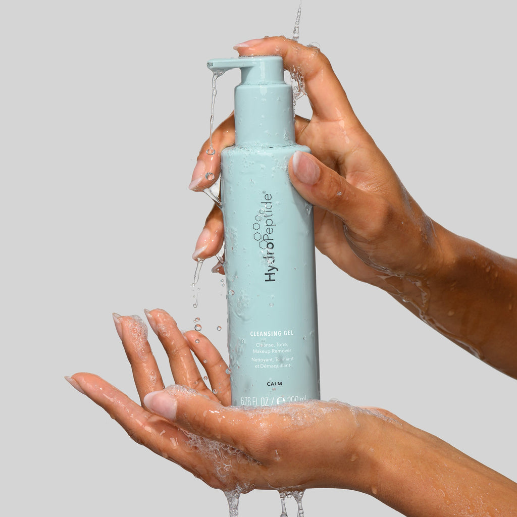 Hand holding a blue bottle labeled 'hydrofluir' with water flowing out against a gray background