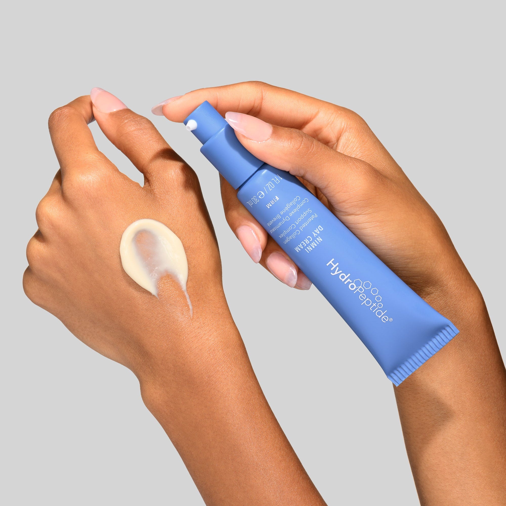 Hand applying a blue skincare product to a wrist with a gray background