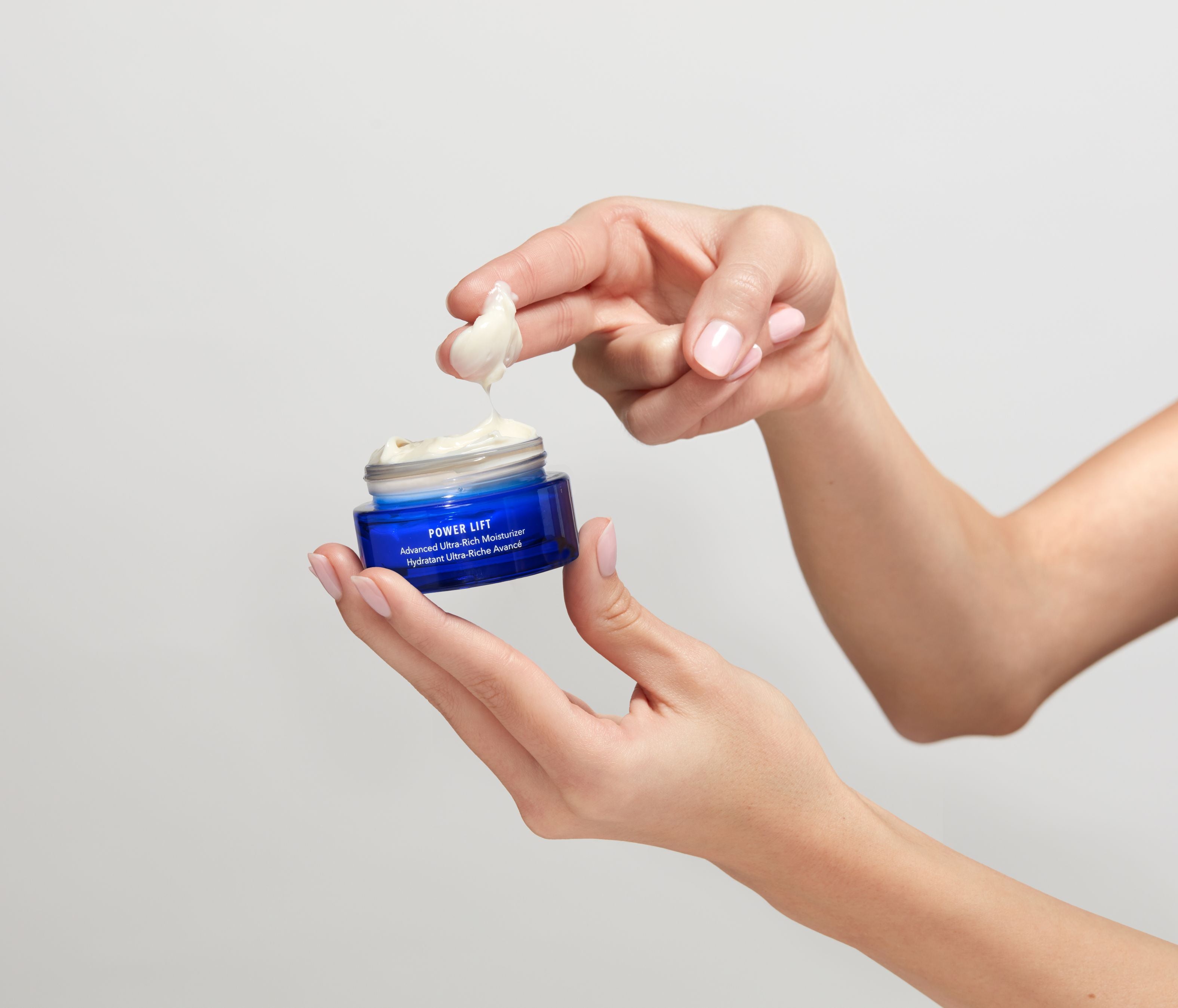 Person applying cream from a blue jar labeled 'Power Lift' on a neutral background