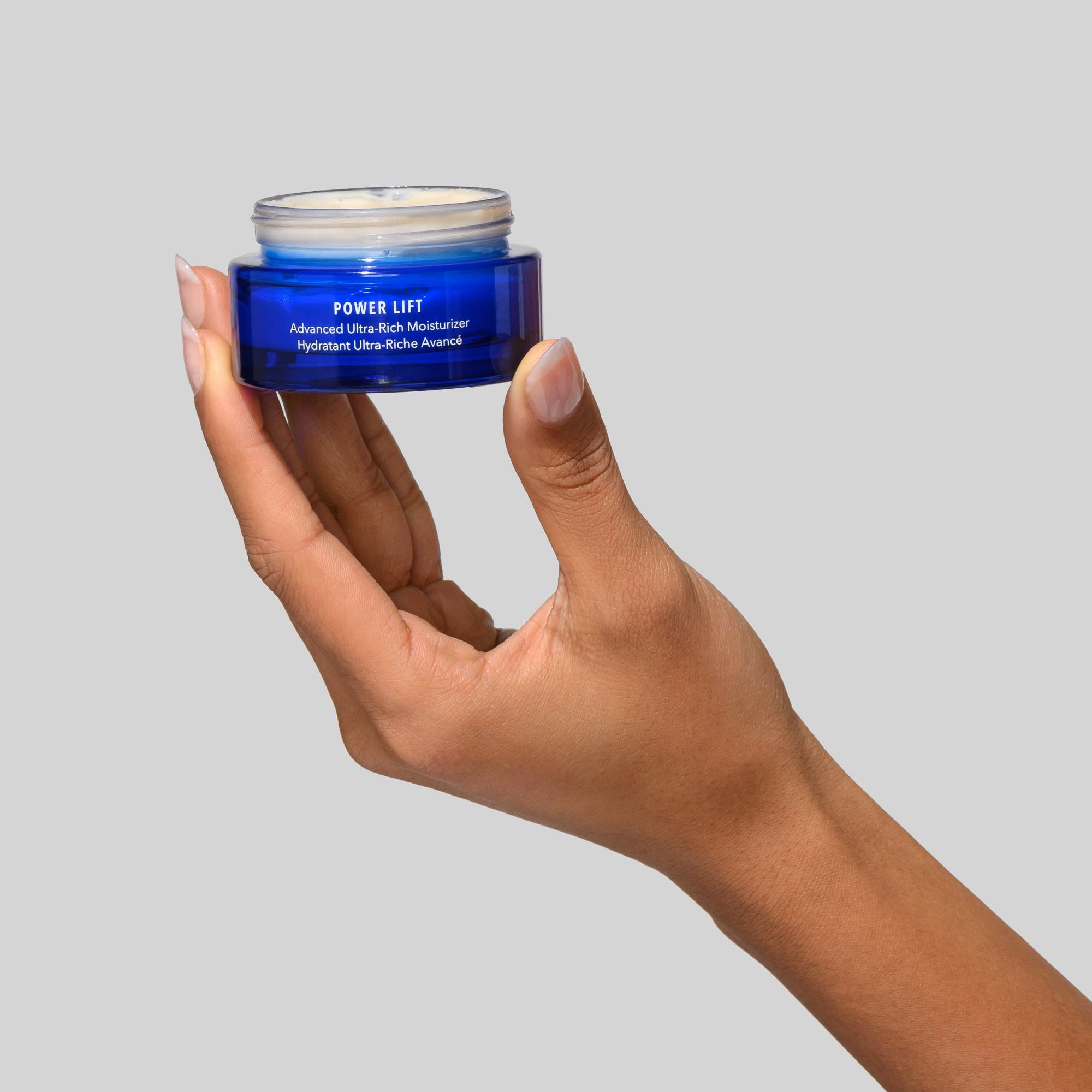 Hand holding a blue jar labeled 'Power Lift' against a gray background